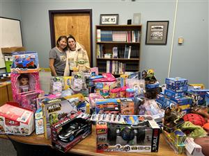 Various toys displayed on a table with two people standing behind it.